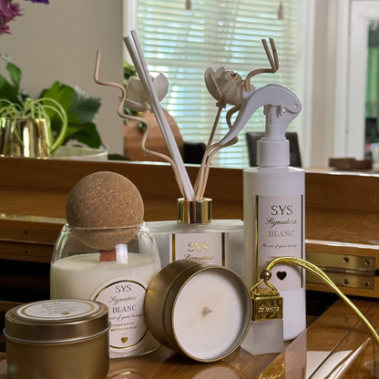 A collection of home fragrance products from SYS Symptimes du Blanc, including reed diffusers, a candle, and a spray bottle, arranged on a polished wooden vanity in a bathroom setting.
